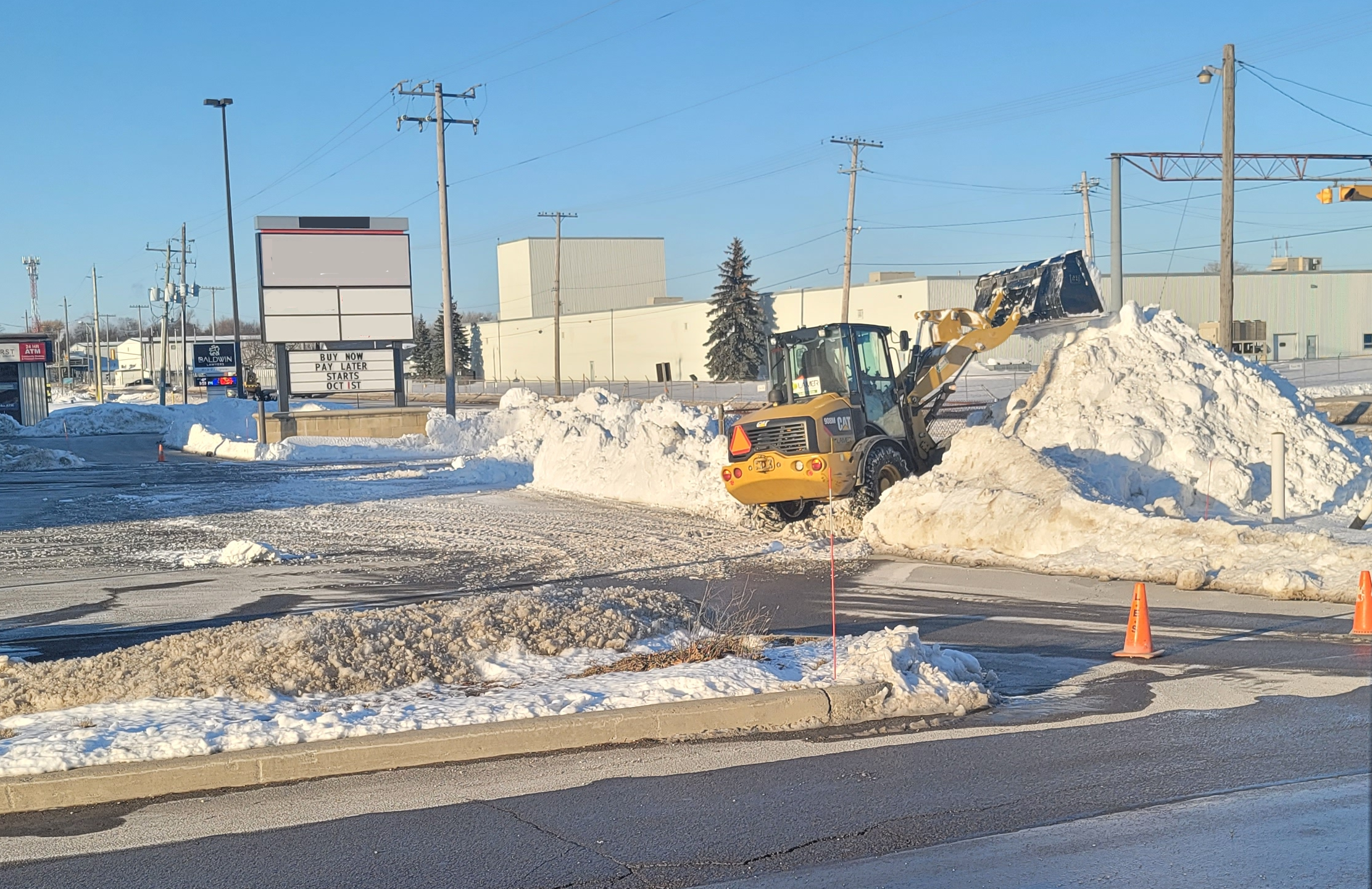 Wheel loader stacking snow beside traffic cones on a commercial property
