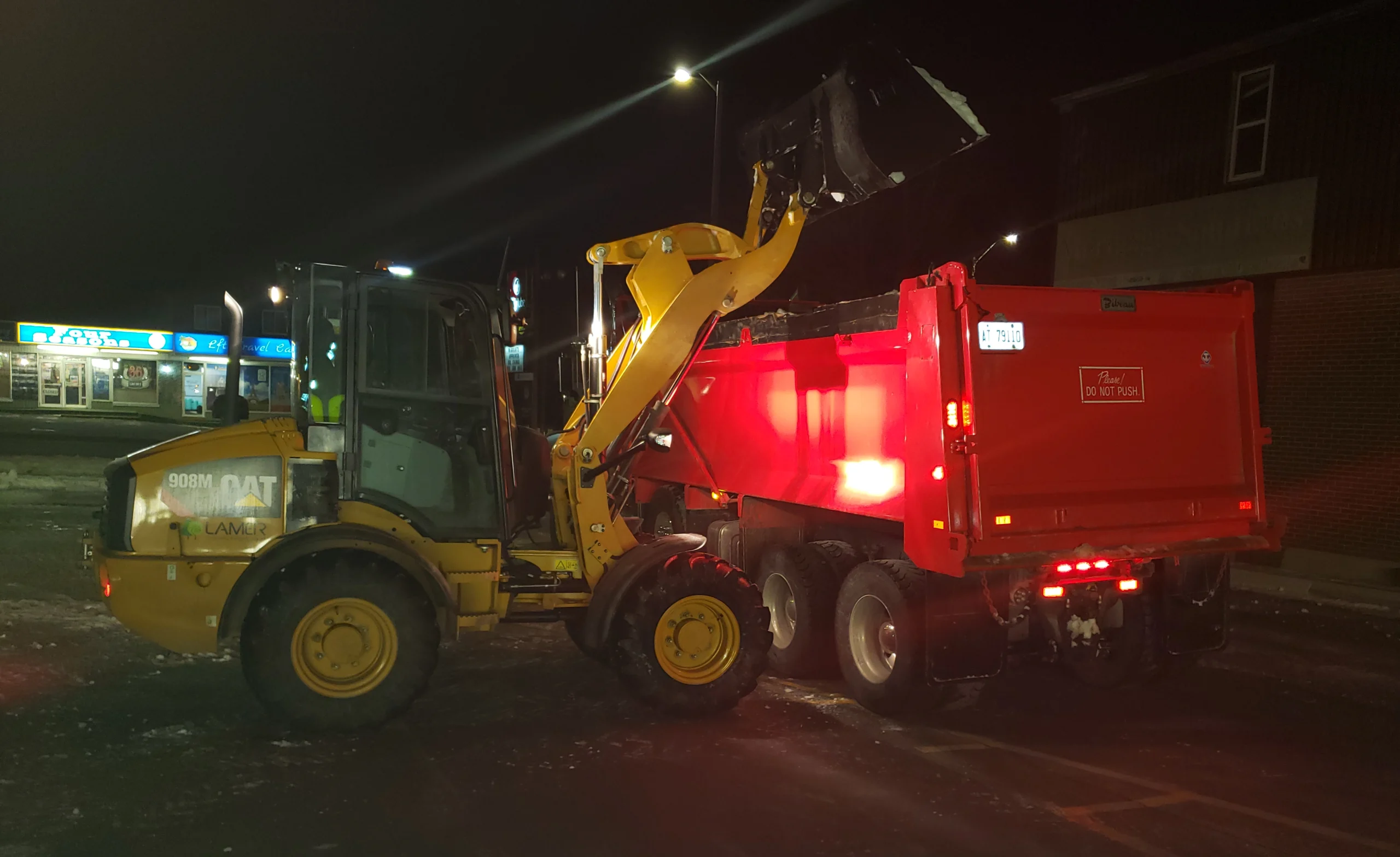 Wheel loader loading cleared snow into a dump truck at night