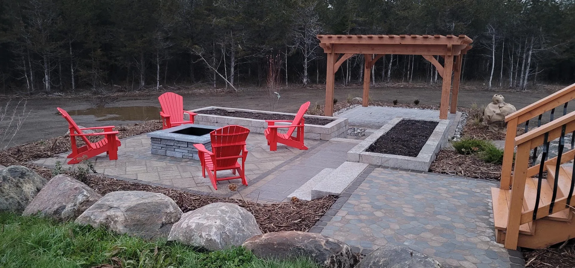 Pergola over a stone fire pit area with red Muskoka chairs
