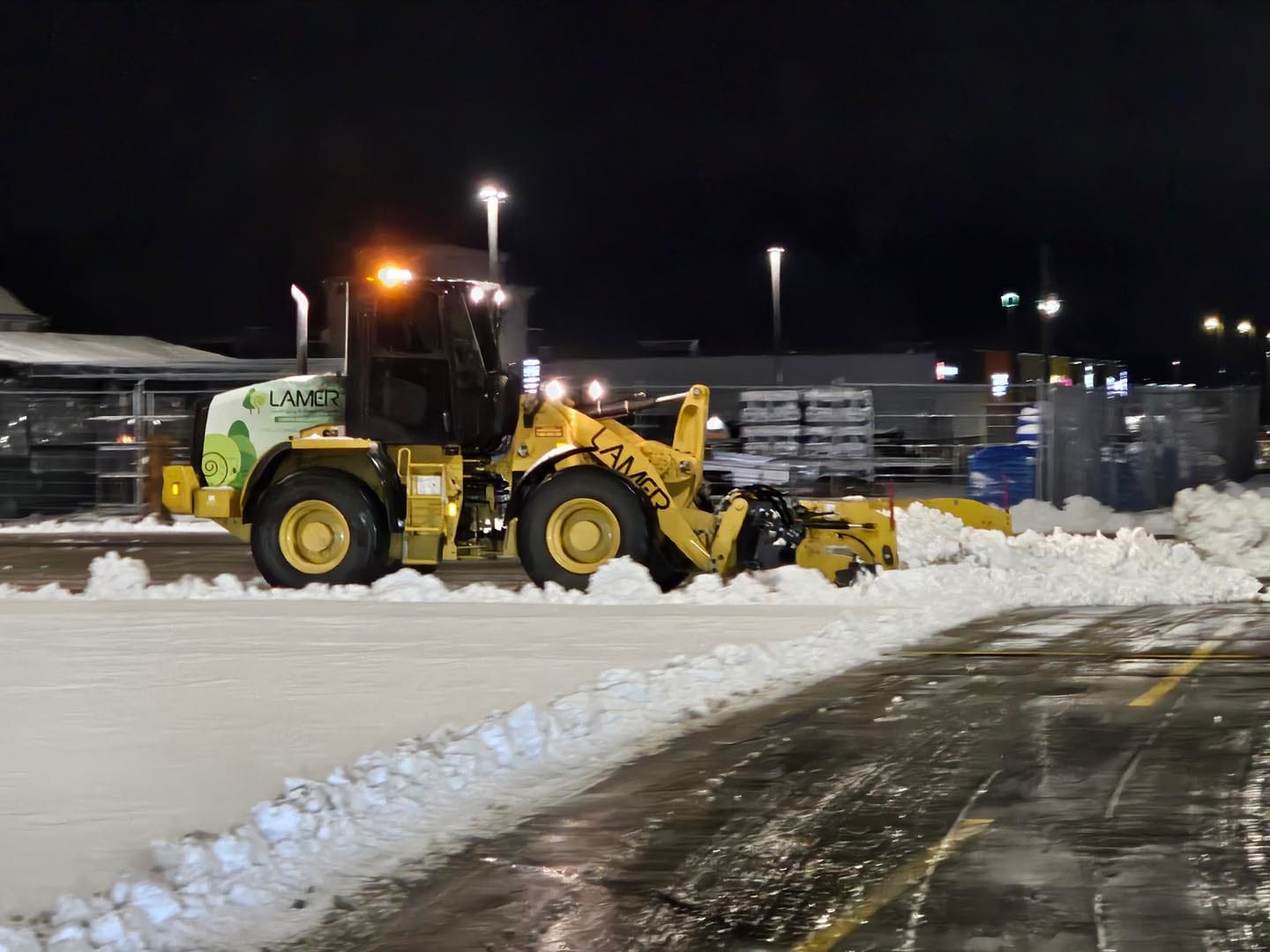 Wheel loader with a snow pusher clearing a lit lot at night