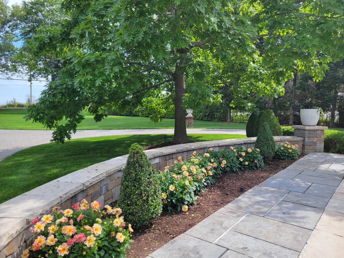 Curved stone walkway with planted beds and a mowed lawn at a residential property