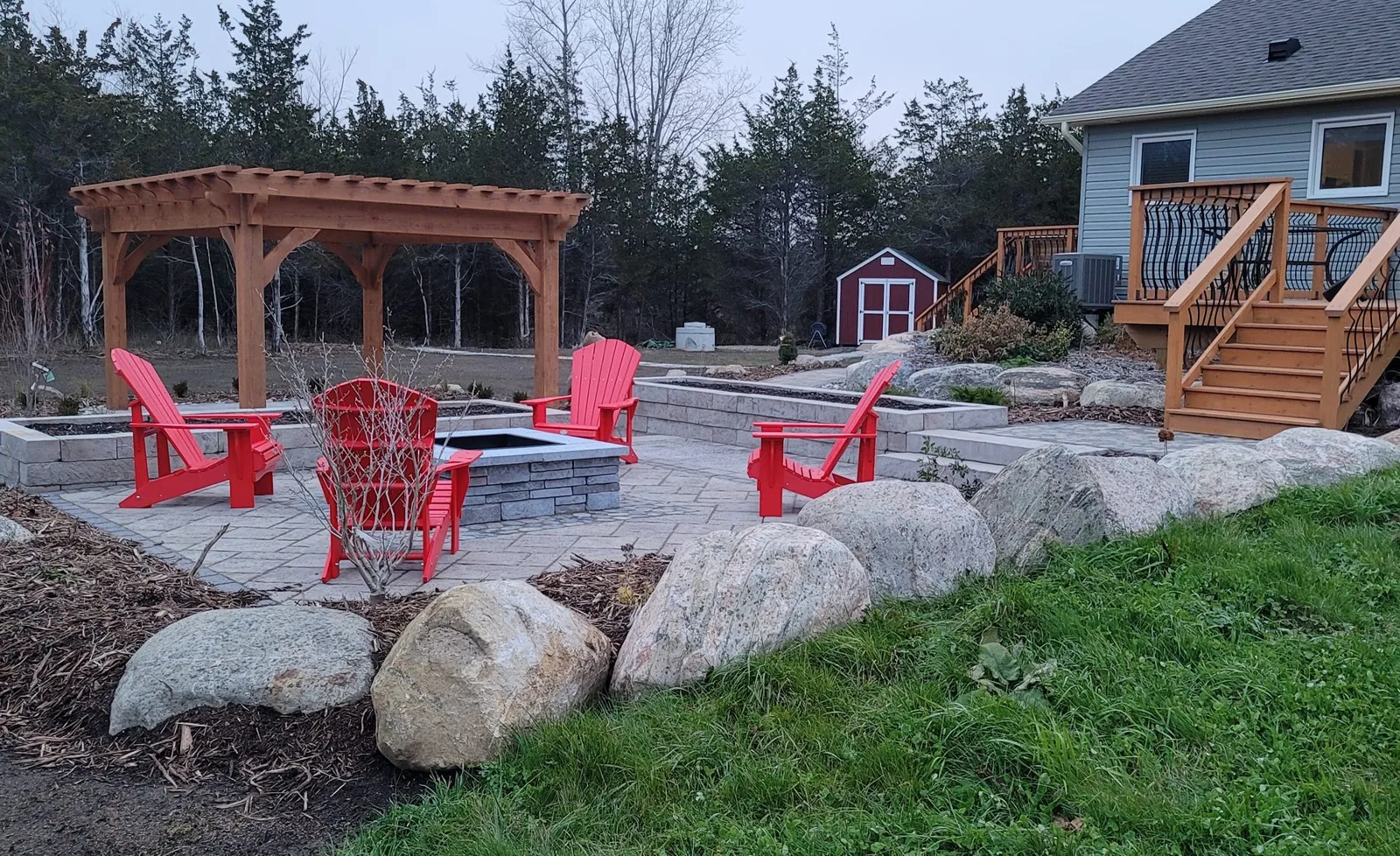 Cedar pergola over a stone fire pit patio with red Muskoka chairs