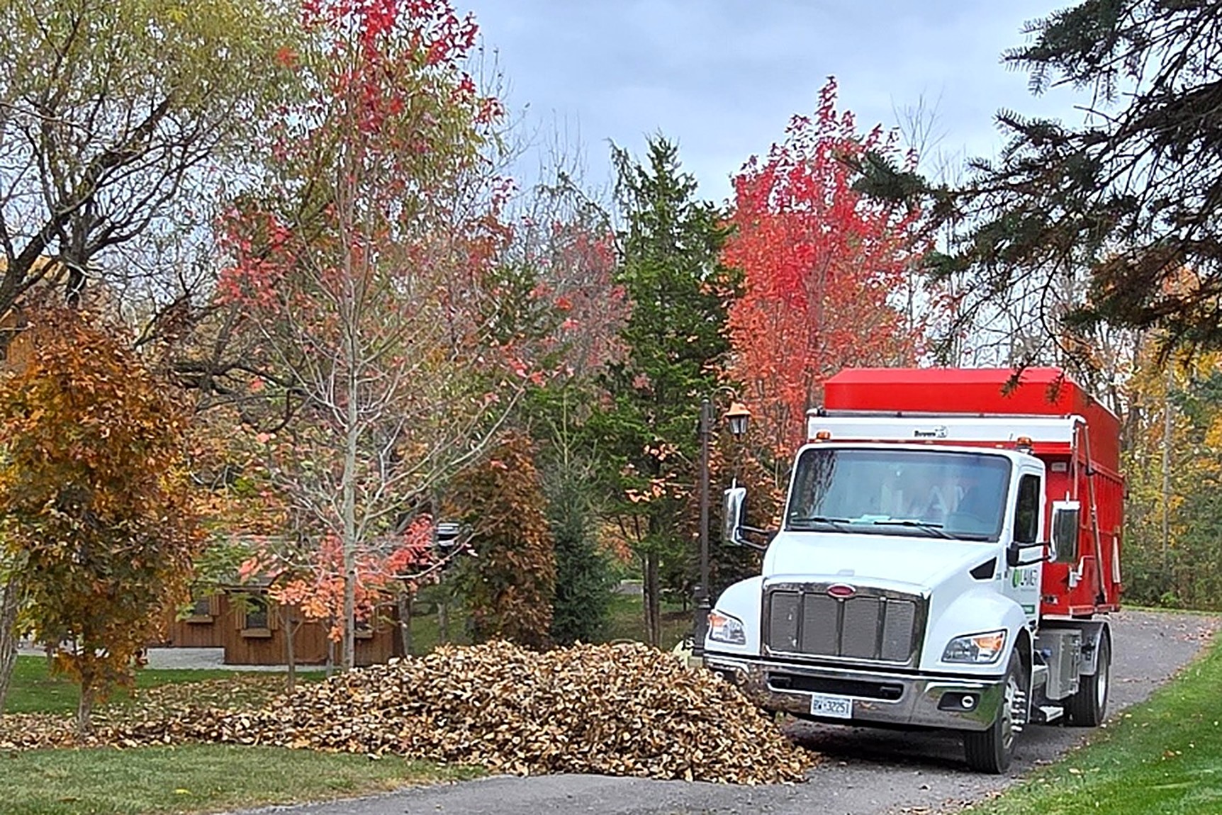 Lamer leaf truck beside a pile of fall leaves on an estate driveway